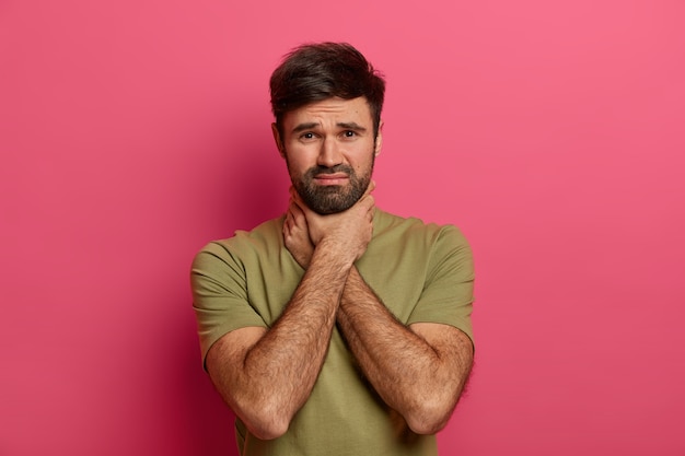 Foto gratuita hombre disgustado sin afeitar mantiene las manos en el cuello, sufre asfixia