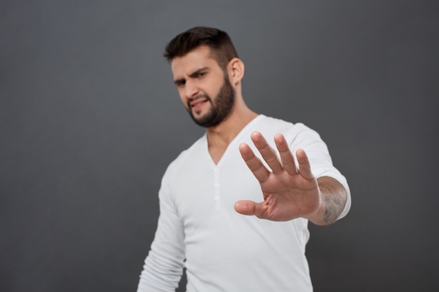 Hombre disgustado negándose, estirando la mano sobre la pared gris