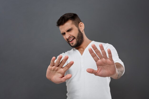 Hombre disgustado negándose, estirando las manos sobre la pared gris