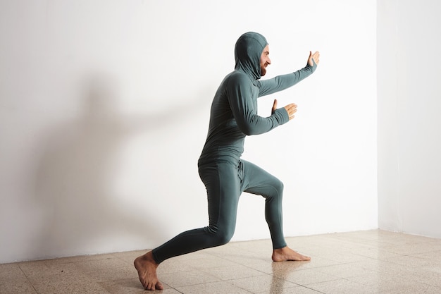 Hombre divertido barbudo posa como un ninja con su suite térmica de capa base térmica, aislado en blanco