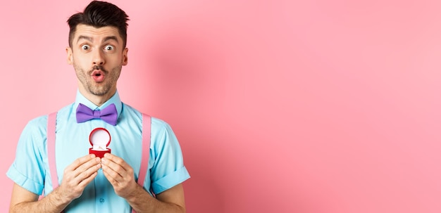 Foto gratuita hombre divertido del día de san valentín con bigote y corbatín que parece emocionado y muestra el anillo de compromiso preguntando