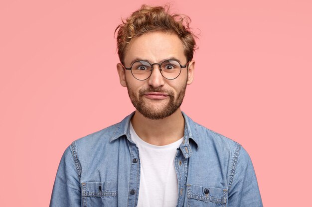 El hombre divertido hace muecas, hace pucheros en los labios, tiene expresión facial cómica, cabello rizado, cerdas