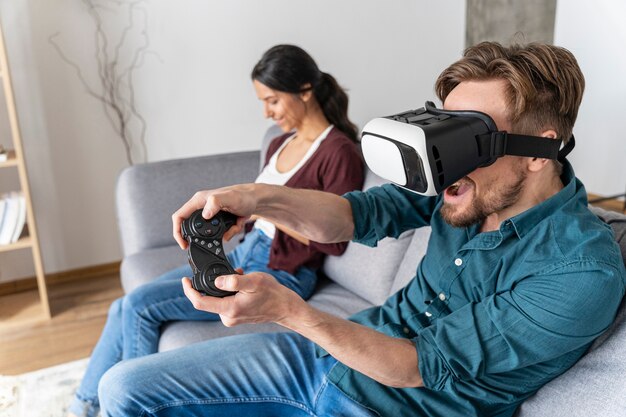 Hombre divirtiéndose en casa en el sofá con casco de realidad virtual jugando videojuegos