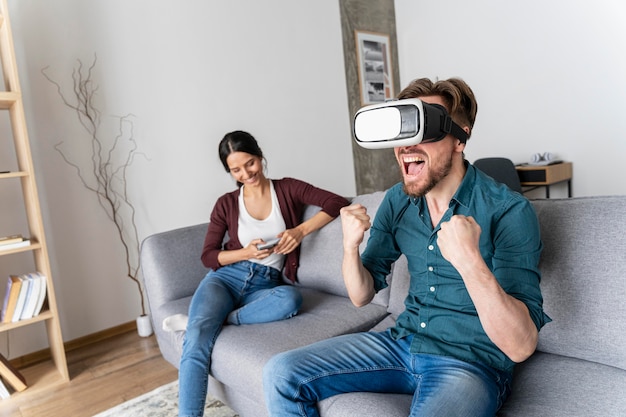 Hombre divirtiéndose en casa en el sofá con casco de realidad virtual