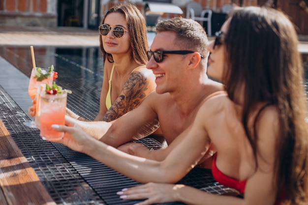 Hombre con dos mujeres en la piscina bebiendo cócteles y divirtiéndose en la piscina