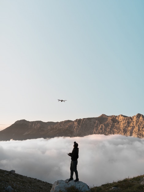 Un hombre con un drone en las montañas volando detrás de las nubes.