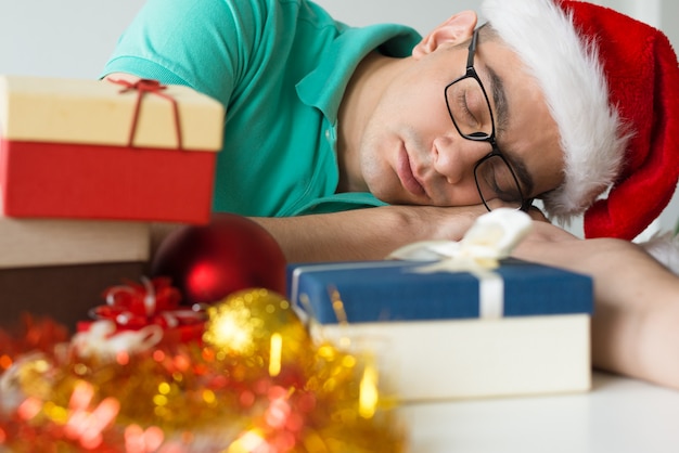 Hombre durmiendo en la mesa con regalos de Navidad y adornos