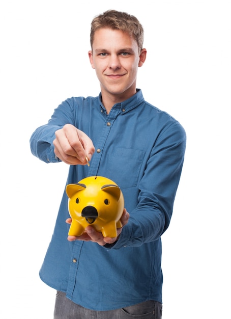 Hombre echando una moneda a una hucha de cerdo amarilla