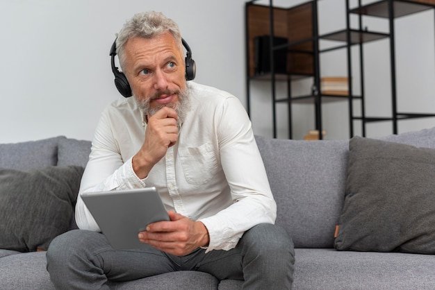 Hombre de edad avanzada con auriculares en casa con dispositivo de tableta