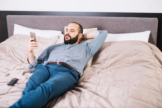 Hombre elegante acostado en la cama con teléfono