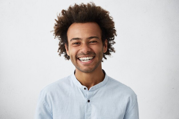 Hombre elegante afroamericano positivo de aspecto amistoso con el pelo y las cerdas funky sonriendo ampliamente
