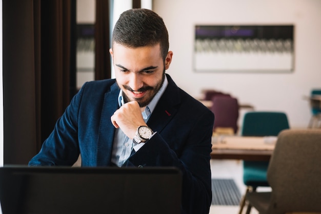 Hombre elegante alegre que usa la computadora portátil