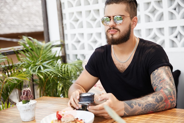 Hombre elegante barbudo sentado en la cafetería