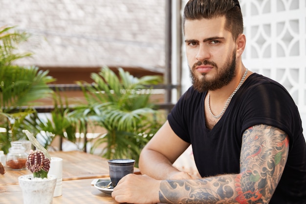 Hombre elegante barbudo sentado en la cafetería