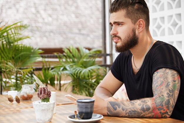 Hombre elegante barbudo sentado en la cafetería