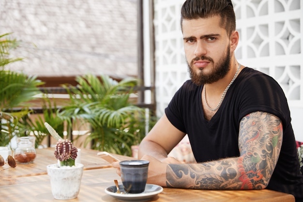 Hombre elegante barbudo sentado en la cafetería