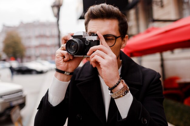 Hombre elegante con cámara de fotos haciendo fotos en ciudad europea.