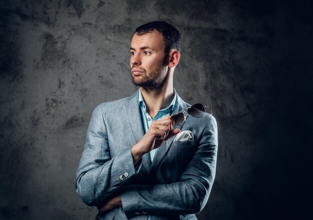 Hombre elegante con chaqueta azul tiene gafas de sol sobre fondo gris.