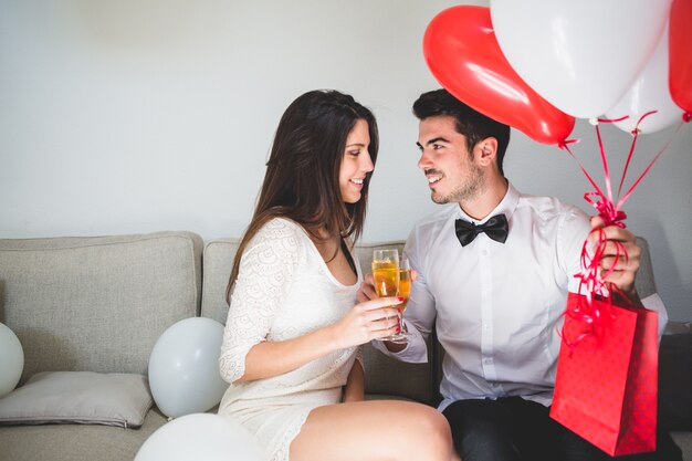 Hombre elegante con globos y una bolsa roja brindando con su novia