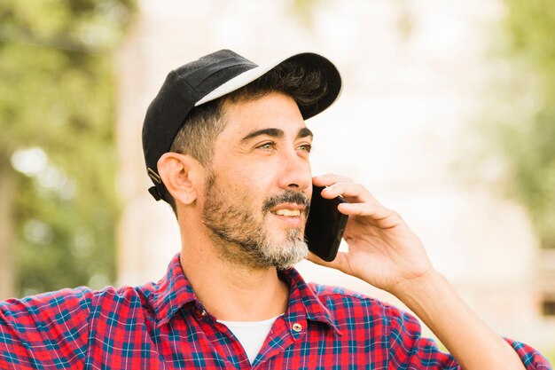 Hombre elegante con gorra negra en la cabeza hablando por teléfono móvil