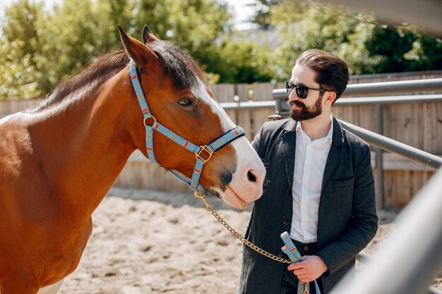 Hombre elegante de pie junto al caballo en un rancho