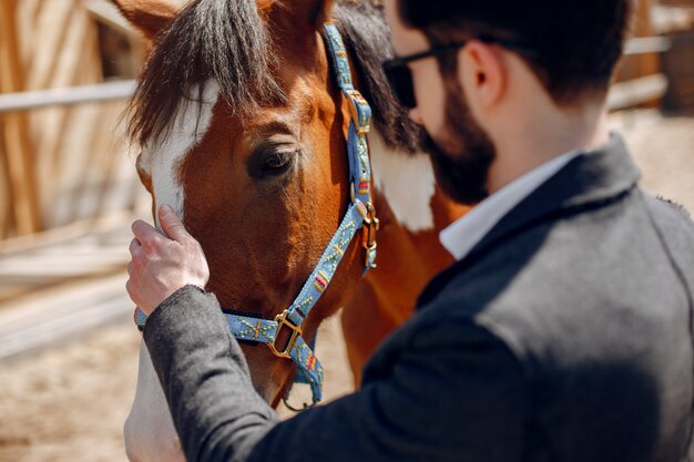 Hombre elegante de pie junto al caballo en un rancho