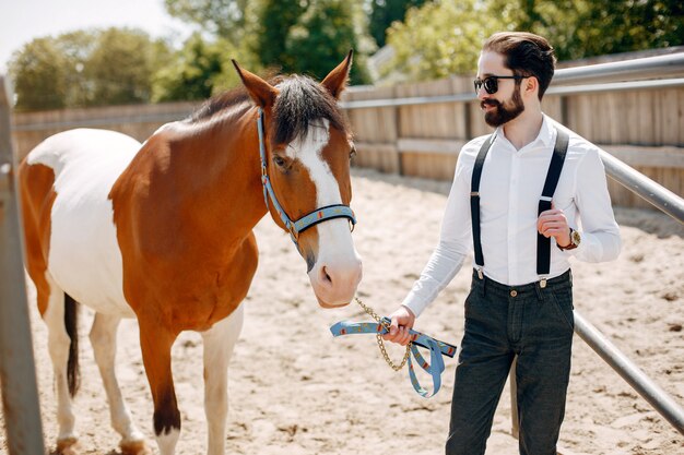Hombre elegante de pie junto al caballo en un rancho