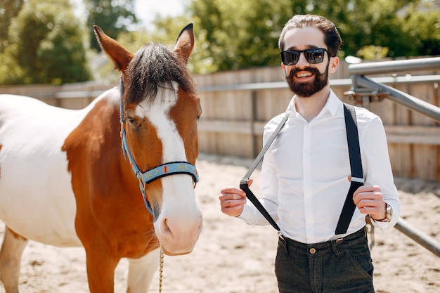 Hombre elegante de pie junto al caballo en un rancho