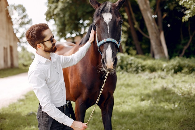 Hombre elegante de pie junto al caballo en un rancho