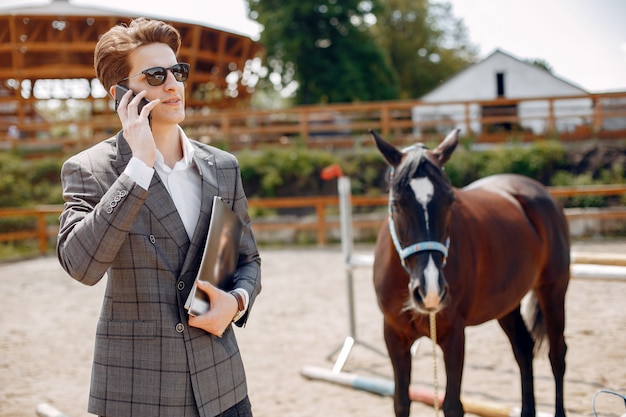 Hombre elegante de pie junto al caballo en un rancho