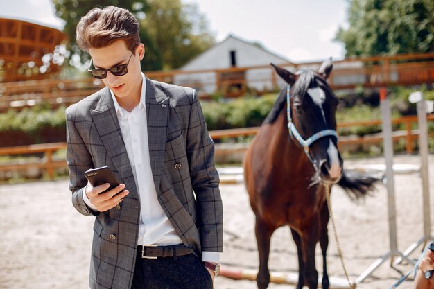 Hombre elegante de pie junto al caballo en un rancho