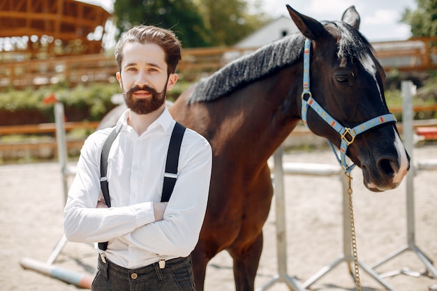 Hombre elegante de pie junto al caballo en un rancho