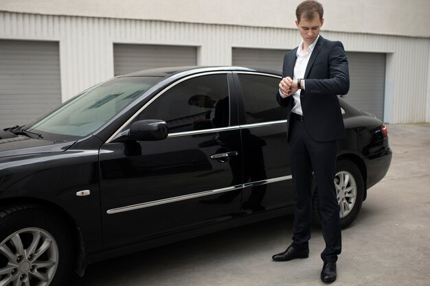 Hombre elegante de pie junto a su coche para servicios de taxi