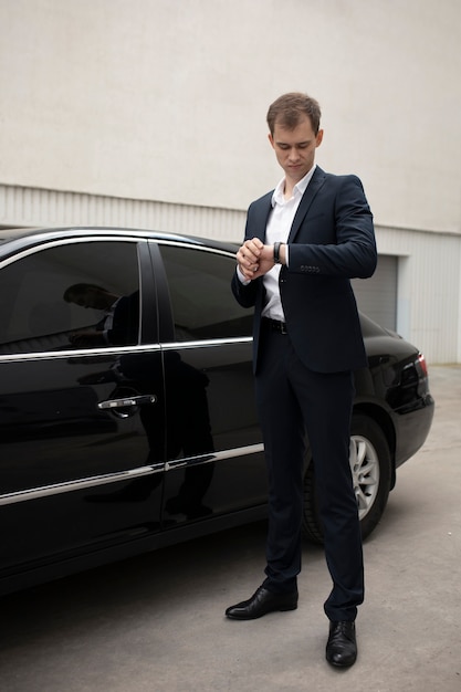 Hombre elegante de pie junto a su coche para servicios de taxi