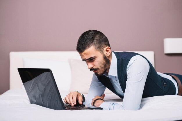 Hombre elegante con portátil posando en la cama