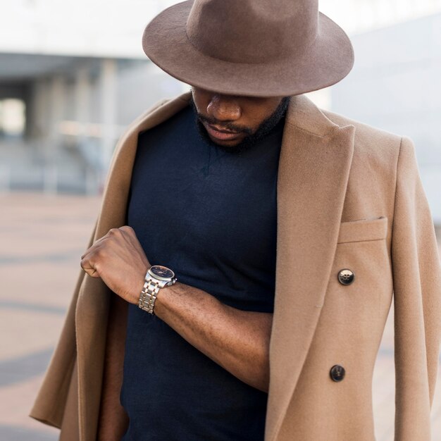 Hombre elegante posando de una manera misteriosa mientras mira su reloj