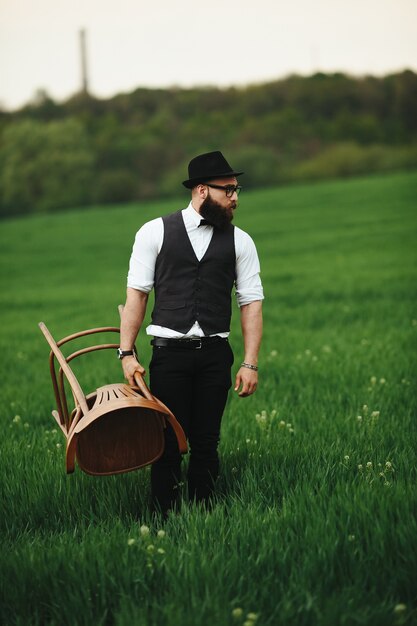 Hombre elegante posando con una silla en el campo