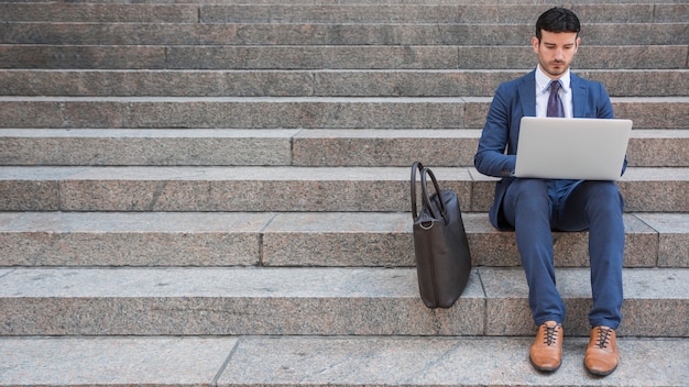 Hombre elegante que usa la computadora portátil en pasos