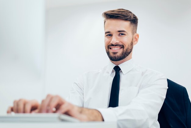 Hombre elegante sonriendo escribiendo en un ordenador