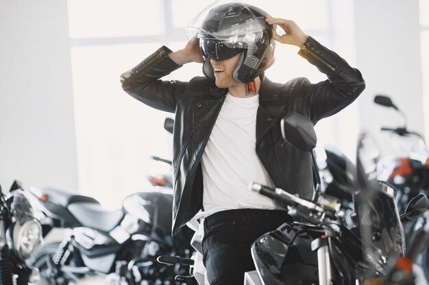 El hombre eligió motocicletas en la tienda de motos. Chico con chaqueta negra. Hombre con casco.