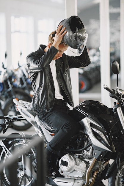 El hombre eligió motocicletas en la tienda de motos. Chico con chaqueta negra. Hombre con casco.