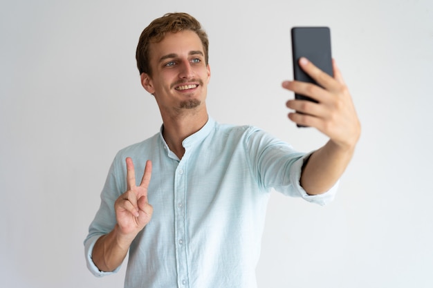 Hombre emocionado feliz que muestra el signo de la paz mientras toma selfie.