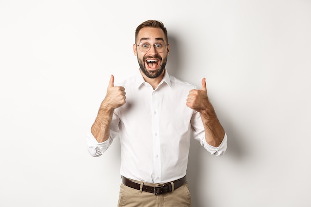 Hombre emocionado con gafas mostrando los pulgares hacia arriba y mirando sorprendido, de acuerdo y aprueba algo genial