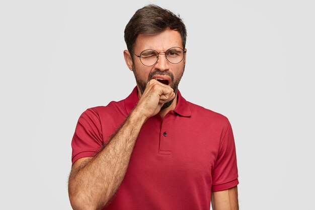 Hombre emocional joven agotado posando contra la pared blanca