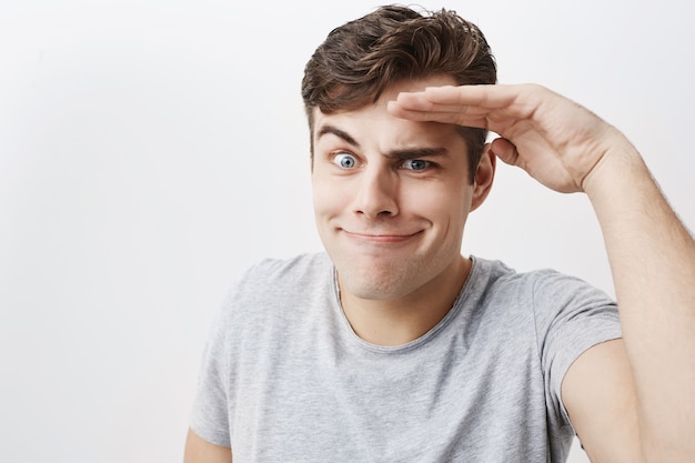 Hombre emocionalmente positivo de ojos azules con cabello oscuro, burlándose, haciendo muecas. Guapo joven apuesto divirtiéndose ondoors. Gestos y expresiones faciales.