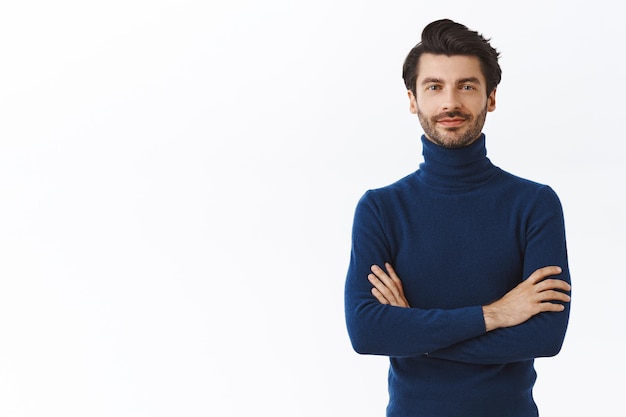 Hombre emprendedor guapo seguro de sí mismo en suéter azul de cuello alto, brazos cruzados sobre el pecho, sonrisa descarada y segura de sí misma