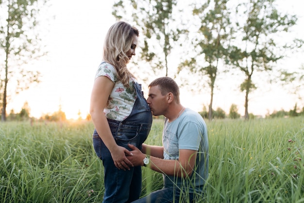 Un hombre encantador está de rodillas ante un vientre de mujer embarazada.