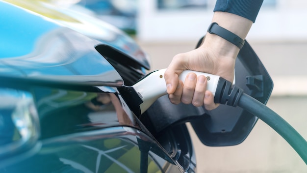 Hombre enchufando el cargador en un coche eléctrico en la estación de carga