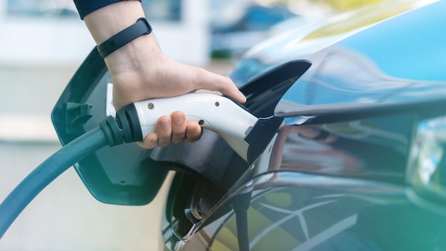 Hombre enchufando el cargador en un coche eléctrico en la estación de carga