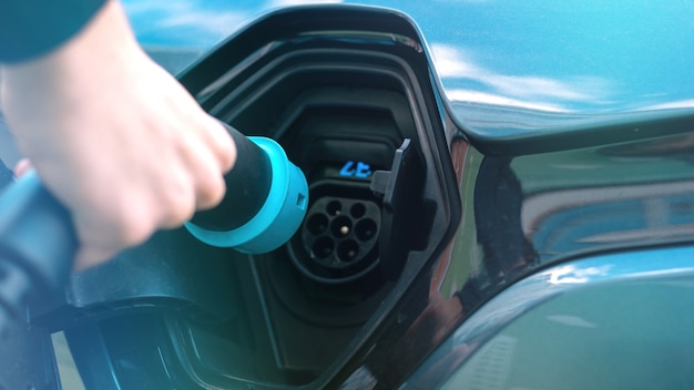 Hombre enchufando el cargador en un coche eléctrico en la estación de carga